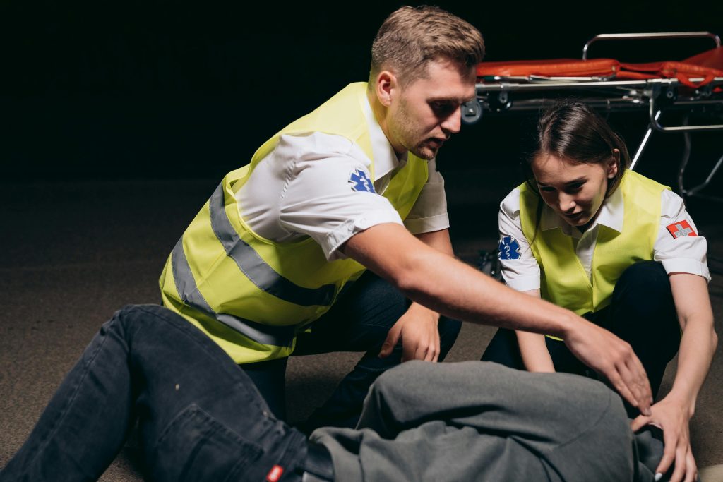 Paramedics providing urgent care to a patient outdoors at night with a stretcher in the background.
